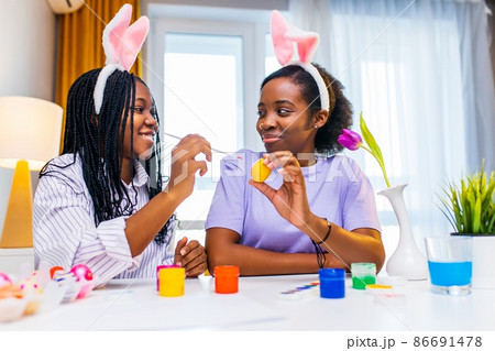 multiracial two women painting eggs with cute pink rabbit costume ears in apartment multiracial two women painting eggs with cute pink rabbit costume ears in apartment 86691478