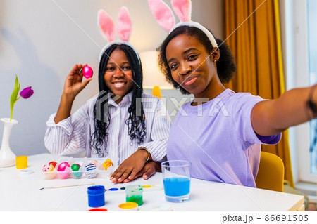 two polyethnic pretty woman taking selfie photo on camera of smartphone and preparing to easter together 86691505