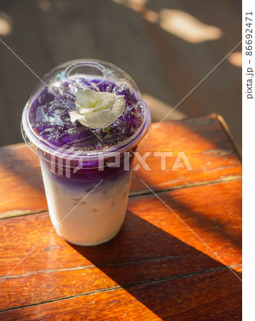 top view butterfly pea milk in a clear plastic glass, placed on a wooden table, on blur nature background top view butterfly pea milk in a clear plastic glass, placed on a wooden table, on blur nature background 86692471