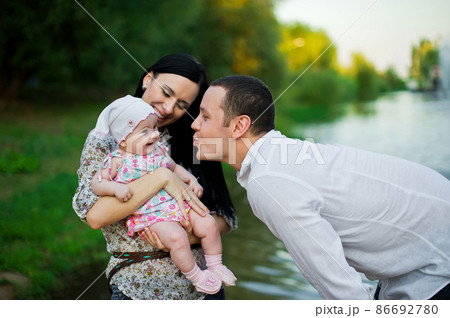 Happy family mother, father, child daughter. Happy young family spending time together outside in green nature. Happy family resting together on the green grass. Happy family having fun outdoors 86692780