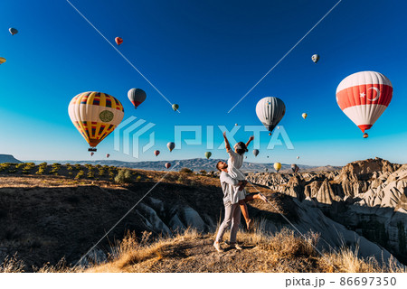 Wedding travel. Honeymoon trip. Couple in love among balloons. A guy proposes to a girl. Couple in love in Cappadocia. Couple in Turkey.  Man and woman traveling. Flying on balloons. Tourists 86697350