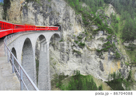 Passenger train goes from Chur to St. Moritz on Landwasser viaduct. Swiss Alps. 86704088
