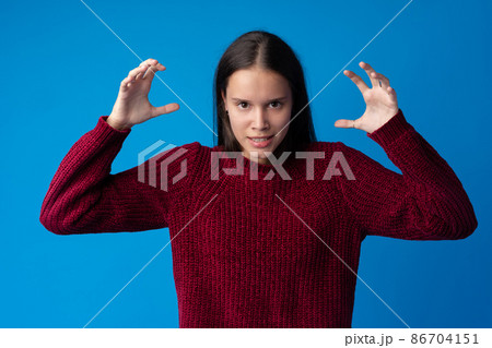 Young annoyed angry woman holding hands in furious gesture on blue background 86704151
