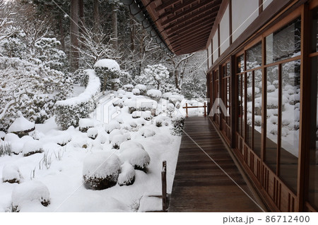 木々の山の中の雪景色の庭の写るガラス窓のある広縁の日本家屋の風景の
