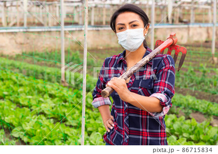 Female farmer in protective mask with rake on a farm field Female farmer in protective mask with rake on a farm field 86715834
