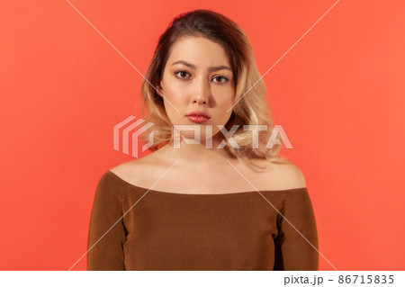 Portrait of unhappy depressed young woman with blonde hair in brown blouse looking at the camera. Her face expressing tiredness and pressure. Indoor isolated on red background, mental health Portrait of unhappy depressed young woman with blonde hair in brown blouse looking at the camera. Her face expressing tiredness and pressure. Indoor isolated on red background, mental health 86715835