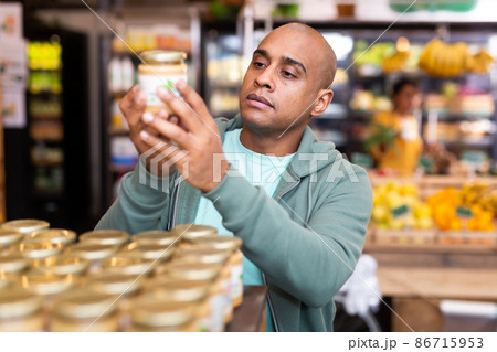 Man reading jar contents on label while shopping in supermarket Man reading jar contents on label while shopping in supermarket 86715953