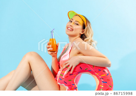 Portrait of beautiful happy woman in bathing suit sitting sexy and smiling to camera, holding rubber ring, fresh juice or cocktail, enjoying rest on summer beach, vacation resort. studio shot isolated Portrait of beautiful happy woman in bathing suit sitting sexy and smiling to camera, holding rubber ring, fresh juice or cocktail, enjoying rest on summer beach, vacation resort. studio shot isolated 86715998
