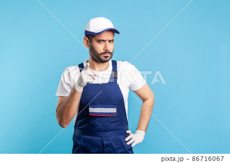 Be careful. Angry handyman in overalls and hygiene gloves standing with admonishing gesture, warning sign. Profession of service industry, courier delivery, housekeeping maintenance. studio shot 86716067