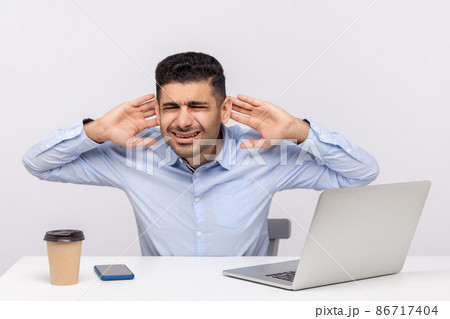 Confused man employee sitting at desk workplace with laptop, holding hands near ears trying to hear better, difficult to listen in noisy office. indoor studio shot isolated on white background Confused man employee sitting at desk workplace with laptop, holding hands near ears trying to hear better, difficult to listen in noisy office. indoor studio shot isolated on white background 86717404
