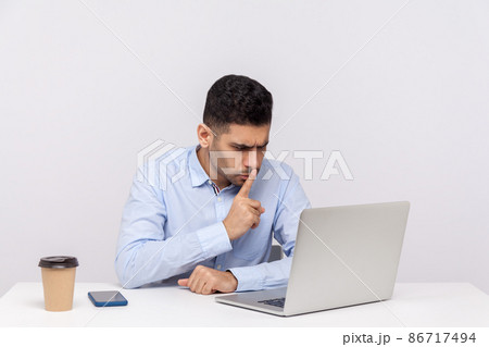 Please, be quiet. Strict bossy man sitting office workplace, asking for silence while talking video call on laptop, keeping finger on lips and hushing. indoor studio shot isolated on white background 86717494