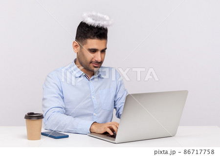 Diligent office worker or top manager sitting at workplace with saint angelic halo on head, working hard attentive on laptop, he has title of best employee. studio shot isolated on white background Diligent office worker or top manager sitting at workplace with saint angelic halo on head, working hard attentive on laptop, he has title of best employee. studio shot isolated on white background 86717758