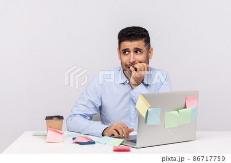 Anxiety disorder, stressful job. Unhappy frustrated man employee sitting in office workplace with sticky notes all around, biting finger nails, nervous about deadline. indoor studio shot isolated Anxiety disorder, stressful job. Unhappy frustrated man employee sitting in office workplace with sticky notes all around, biting finger nails, nervous about deadline. indoor studio shot isolated 86717759