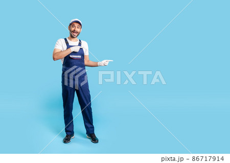 Full length surprised handyman in uniform pointing at copy space, advertising area for idea presentation, looking shocked at camera. Profession of service industry, builder or contractor. isolated 86717914