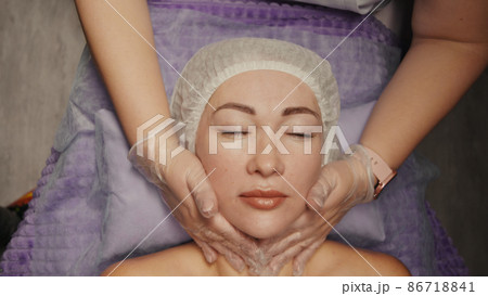 Woman receiving anti-ageing facial massage in spa salon relax. Wellness body skin care face beauty treatment. Black background Woman receiving anti-ageing facial massage in spa salon relax. Wellness body skin care face beauty treatment. Black background 86718841