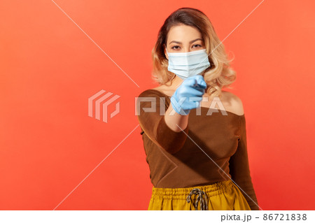 Portrait of strict woman wearing hygienic face mask and gloves, pointing finger to camera, giving recommendations to prevent coronavirus disease, 2019-ncov pandemic threat. indoor studio shot isolated Portrait of strict woman wearing hygienic face mask and gloves, pointing finger to camera, giving recommendations to prevent coronavirus disease, 2019-ncov pandemic threat. indoor studio shot isolated 86721838