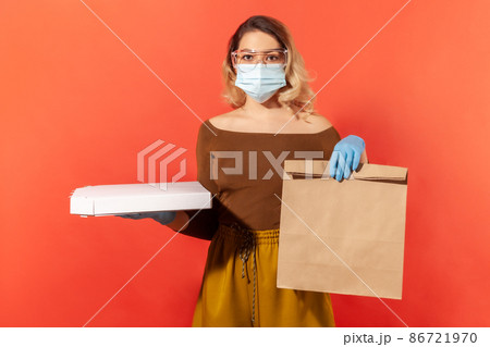 Safe food shopping on quarantine. Woman in protective mask, gloves, glasses holding groceries bag and pizza, delivery service in coronavirus self-isolation, online order. indoor studio shot, isolated 86721970