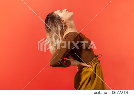 Backache. Side view portrait of unhealthy woman screaming in acute pain and holding sore back, risk of kidney stones disease, pinched nerve. Indoor studio shot isolated on red background Backache. Side view portrait of unhealthy woman screaming in acute pain and holding sore back, risk of kidney stones disease, pinched nerve. Indoor studio shot isolated on red background 86722142