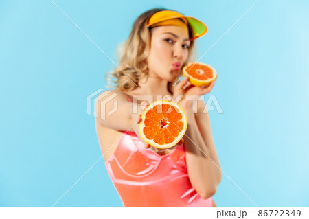 Portrait of beautiful woman in swimsuit giving fresh cut orange to camera and sending air kiss with pout lips. Concept of female beauty, natural healthy nutrition, dietary fruits. studio shot isolated Portrait of beautiful woman in swimsuit giving fresh cut orange to camera and sending air kiss with pout lips. Concept of female beauty, natural healthy nutrition, dietary fruits. studio shot isolated 86722349