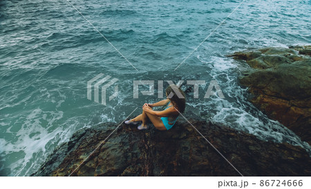 Woman walk near a rock reef hill in stormy morning rain cloudy sea. Concept resort outdoor relax, vacation, loneliness Woman walk near a rock reef hill in stormy morning rain cloudy sea. Concept resort outdoor relax, vacation, loneliness 86724666