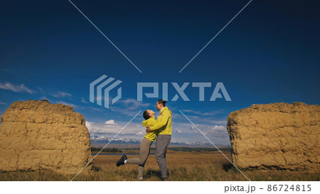 Man and woman in yellow green sportswear. Lovely couple of travelers hug and kiss near old stone enjoying highland landscape. Man and woman in yellow green sportswear. Lovely couple of travelers hug and kiss near old stone enjoying highland landscape. 86724815