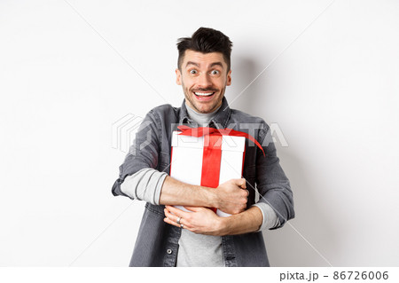 Happy caucasian man holding surprise gift, hugging present and smiling thankful, looking at camera with love and appreciation, celebrate valentines holiday, white background Happy caucasian man holding surprise gift, hugging present and smiling thankful, looking at camera with love and appreciation, celebrate valentines holiday, white background 86726006