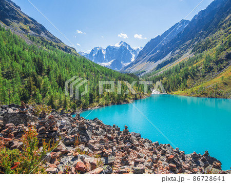Amazing clear mountain lake in forest among fir trees in sunshine. Bright scenery with beautiful turquoise lake against the background of snow-capped mountains. Lower Shavlin Lake 86728641