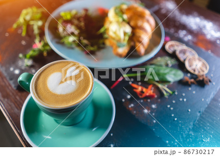 croissant sandwich breakfast with green salad and poached eggs, bacon and coffee 86730217