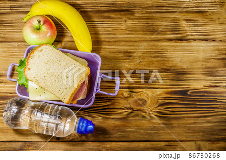 Lunch box with sandwiches, bottle of water, banana and apple on a wooden table. Top view, copy space 86730268