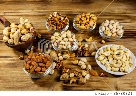 Assortment of nuts on wooden table. Almond, hazelnut, pistachio, peanut, walnut and cashew in small bowls. Healthy eating concept 86730321
