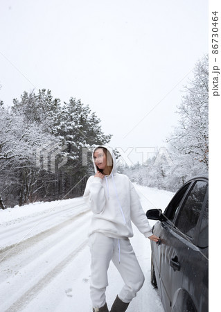 young woman opens the door to the car against the backdrop of a snowy landscape 86730464