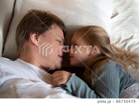 little cute girl hugging her dad while lying in bed little cute girl hugging her dad while lying in bed 86730479