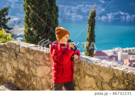 Young tourist boy enjoying a view of Kotor Bay, Montenegro. Kotor Old Town Ladder of Kotor Fortress Hiking Trail. Aerial drone view 86732235