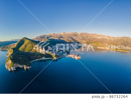 Aerial view of Sveti Nikola, Budva island, Montenegro. Hawaii beach, umbrellas and bathers and crystal clear waters. Jagged coasts with sheer cliffs overlooking the transparent sea. Wild nature 86732264