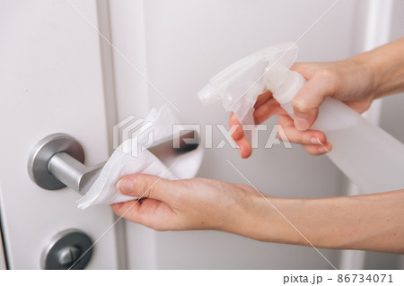 Cleaning white door handles with an antiseptic wet wipe and sanitizer spray. Disinfection in hospital and public spaces against corona virus. Woman hand using towel for cleaning home room door link. Cleaning white door handles with an antiseptic wet wipe and sanitizer spray. Disinfection in hospital and public spaces against corona virus. Woman hand using towel for cleaning home room door link. 86734071