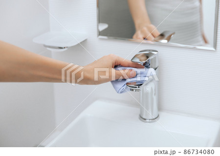 Cleaning the sink faucet with a microfiber cloth. Cleaning the bathroom. Sanitize surfaces prevention in hospital and public spaces against corona virus. Woman hand using wet wipe. 86734080