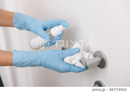 Cleaning black door handle with an antiseptic wet wipe, blue gloves and sanitizer. Woman hand using towel for cleaning. Sanitize surfaces prevention in hospital and public spaces against corona virus. Cleaning black door handle with an antiseptic wet wipe, blue gloves and sanitizer. Woman hand using towel for cleaning. Sanitize surfaces prevention in hospital and public spaces against corona virus. 86734082
