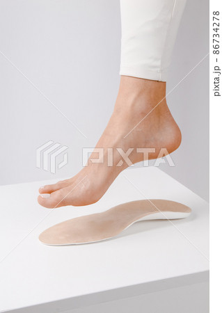 Medical insoles. Isolated orthopedic insoles on a white background. Treatment and prevention of flat feet and foot diseases. Foot care. Insole cutaway layers. Leg hanging over the insole. 86734278