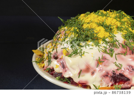 Herring under a fur coat with mayonnaise in a white plate on the table with a reflection. Herring under a fur coat with mayonnaise in a white plate on the table with a reflection. 86738139