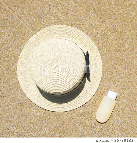 Summer straw hat and sunscreen lying on sand of beach. Travel, holiday, summertime concept. Copy space. Top view. Flat lay Summer straw hat and sunscreen lying on sand of beach. Travel, holiday, summertime concept. Copy space. Top view. Flat lay 86739132