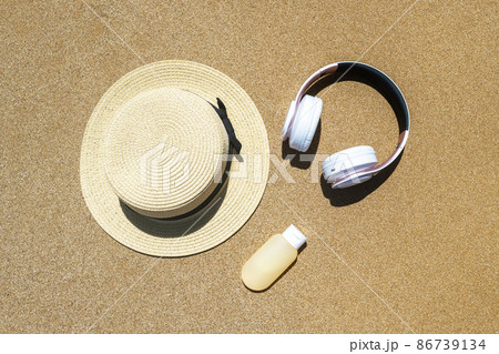 Summer straw hat, headphones and sunscreen lying on sand of beach. Travel, holiday, summertime concept. Copy space. Top view. Flat lay 86739134