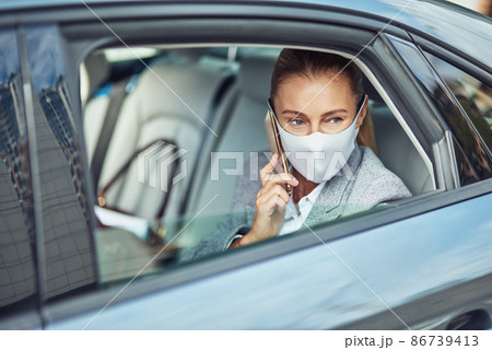 Covid 19 or coronavirus outbreak, caucasian businesswoman wearing medical protective mask talking on smartphone while sitting on back seat in the car, looking out of a window Covid 19 or coronavirus outbreak, caucasian businesswoman wearing medical protective mask talking on smartphone while sitting on back seat in the car, looking out of a window 86739413