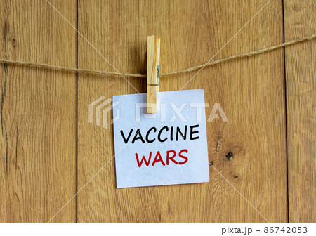 COVID-19 vaccine wars symbol. White paper with text 'vaccine wars', clip on wood clothespin. Beautiful wooden background. COVID-19 vaccine wars concept. COVID-19 vaccine wars symbol. White paper with text 'vaccine wars', clip on wood clothespin. Beautiful wooden background. COVID-19 vaccine wars concept. 86742053