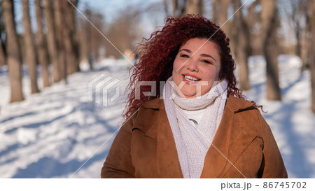 Portrait of a red-haired curly fat woman in the park in winter. Portrait of a red-haired curly fat woman in the park in winter. 86745702