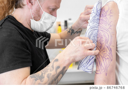 Skilled Tattoo artist putting a sketch on the arm of a man. 86746768
