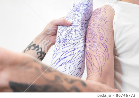 Skilled Tattoo artist putting a sketch on the arm of a man. Skilled Tattoo artist putting a sketch on the arm of a man. 86746772
