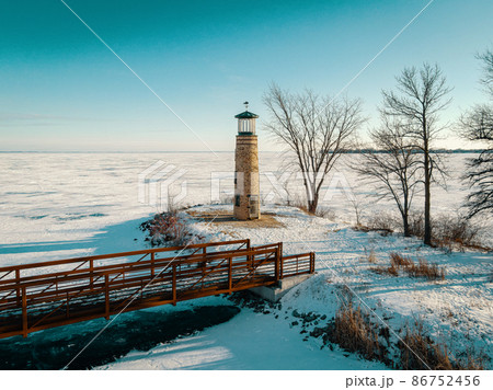 The land and water is frozen with snow coverings. This old light house at a park stands watch. 86752456