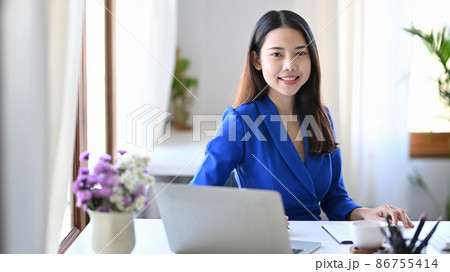 Gorgeous businesswoman siting at comfortable workplace and smiling at camera. Gorgeous businesswoman siting at comfortable workplace and smiling at camera. 86755414