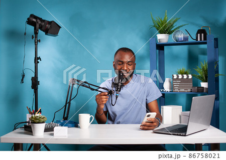 Vlogger holding smartphone looking at screen reading questions from fans using microphone 86758021