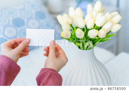 Woman pulling blank greeting card from bouquet of white tulips flowers. Mother day, Copy space. Mock up 86758500